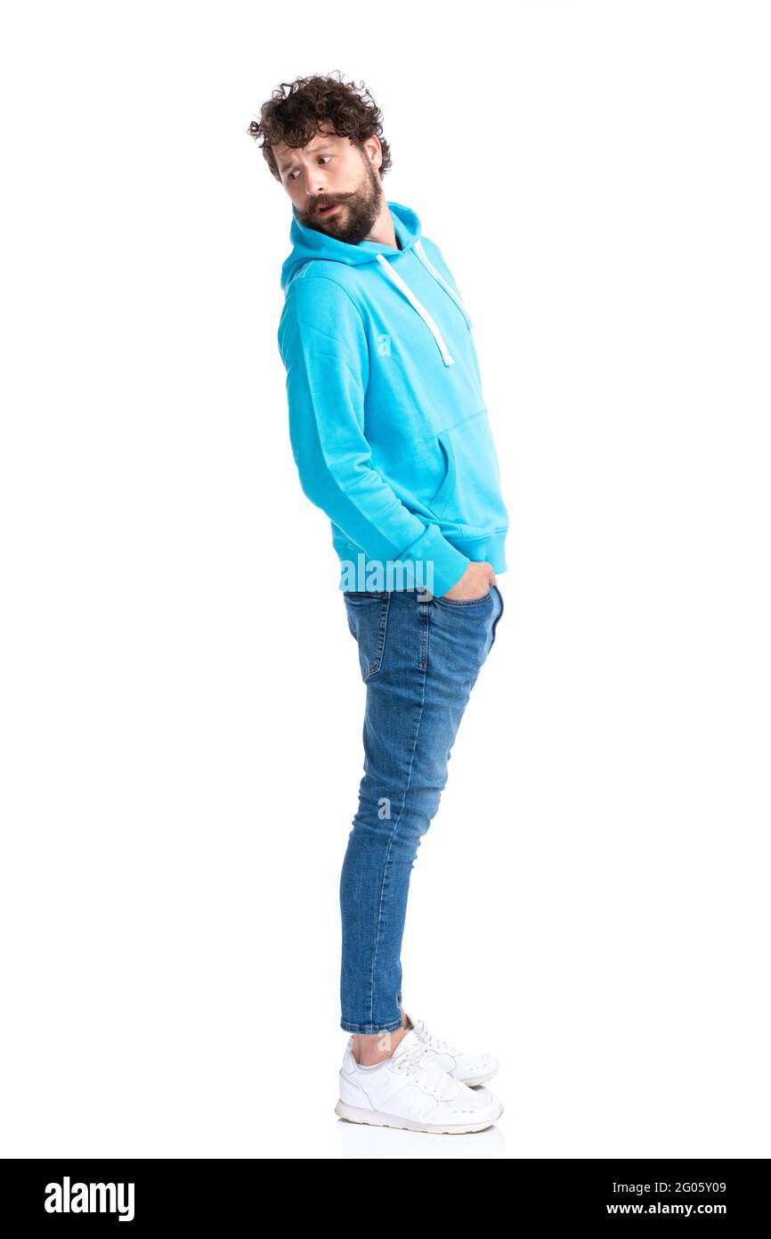 Lässiges Modelmodell in blauem Hoodie, das die Hände in den Taschen hält und neugierig über die Schulter blickt, während es im Studio auf weißem Hintergrund in einer Schlange wartet Stockfoto