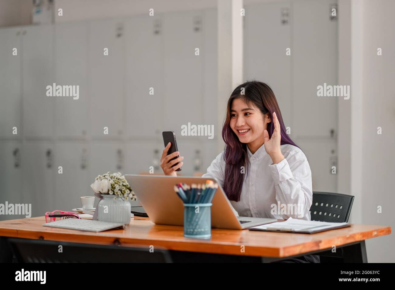 Glückliche junge asiatische Frau hält Telefon Blick auf den Bildschirm winkende Hand Video Anruf Distanz Freund online in mobilen Chat-App mit Smartphone-Videochat Stockfoto
