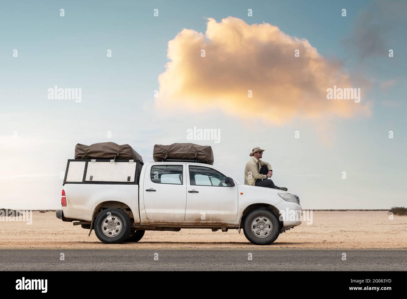 Ein Tourist sitzt in seinem SUV mit Zelten auf einer Straße in der namibischen Wüste in Afrika. Safari-Expedition und Reise-Abenteuer-Konzept Stockfoto