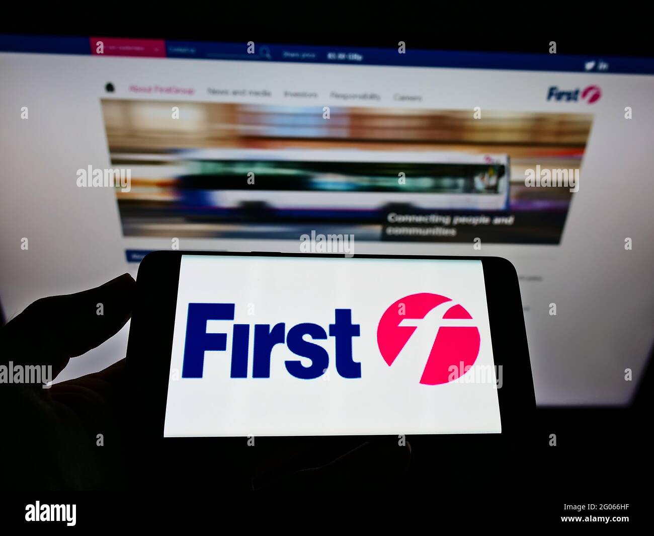 Person mit Mobiltelefon und Logo des britischen Transportunternehmens FirstGroup plc auf dem Bildschirm vor der Business-Webseite. Konzentrieren Sie sich auf die Telefonanzeige. Stockfoto