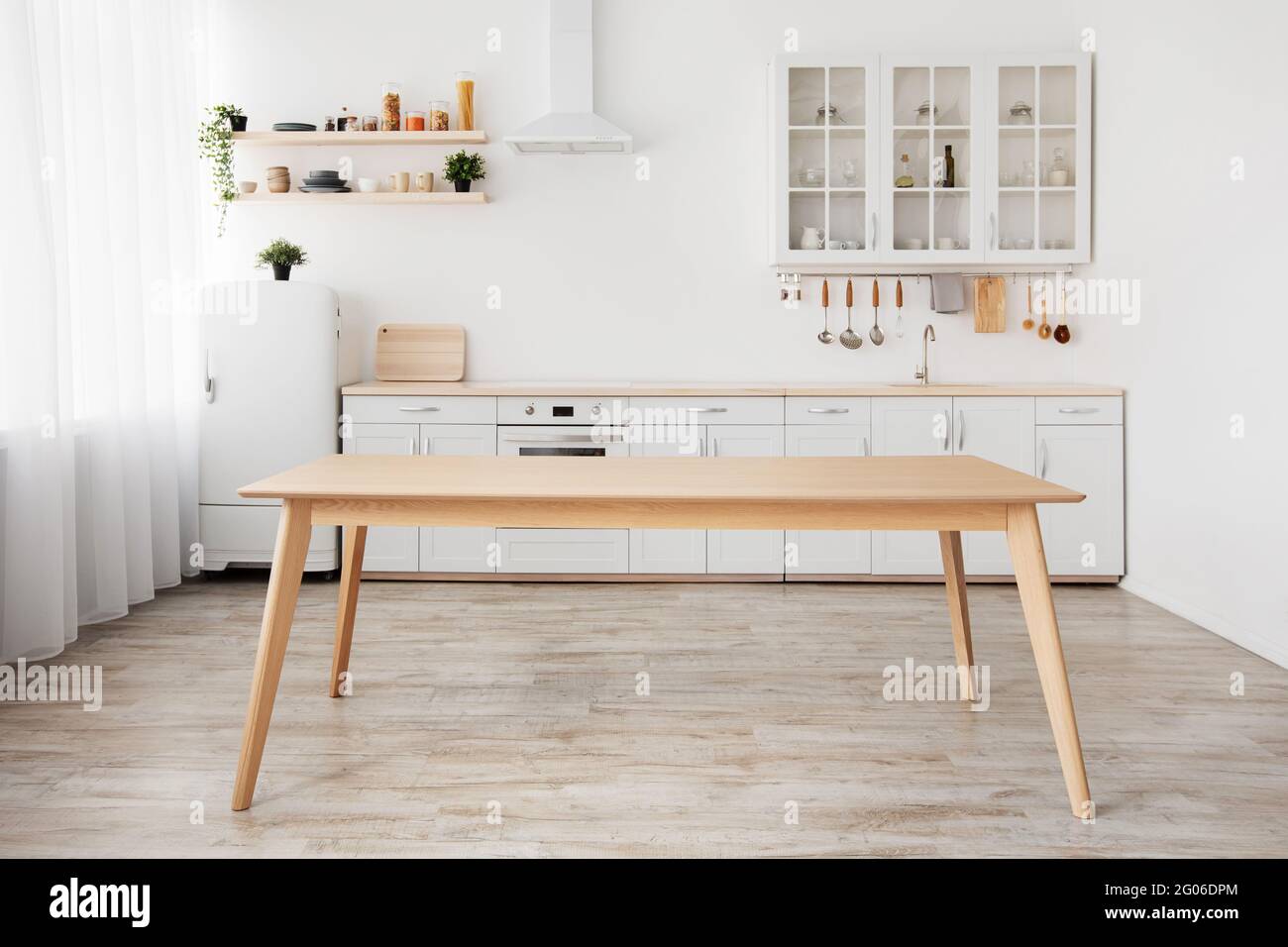 Esszimmer und minimalistisches Design der Küche. Leerer Holztisch, weiße Möbel und verschiedene Utensilien, kleiner Kühlschrank Stockfoto