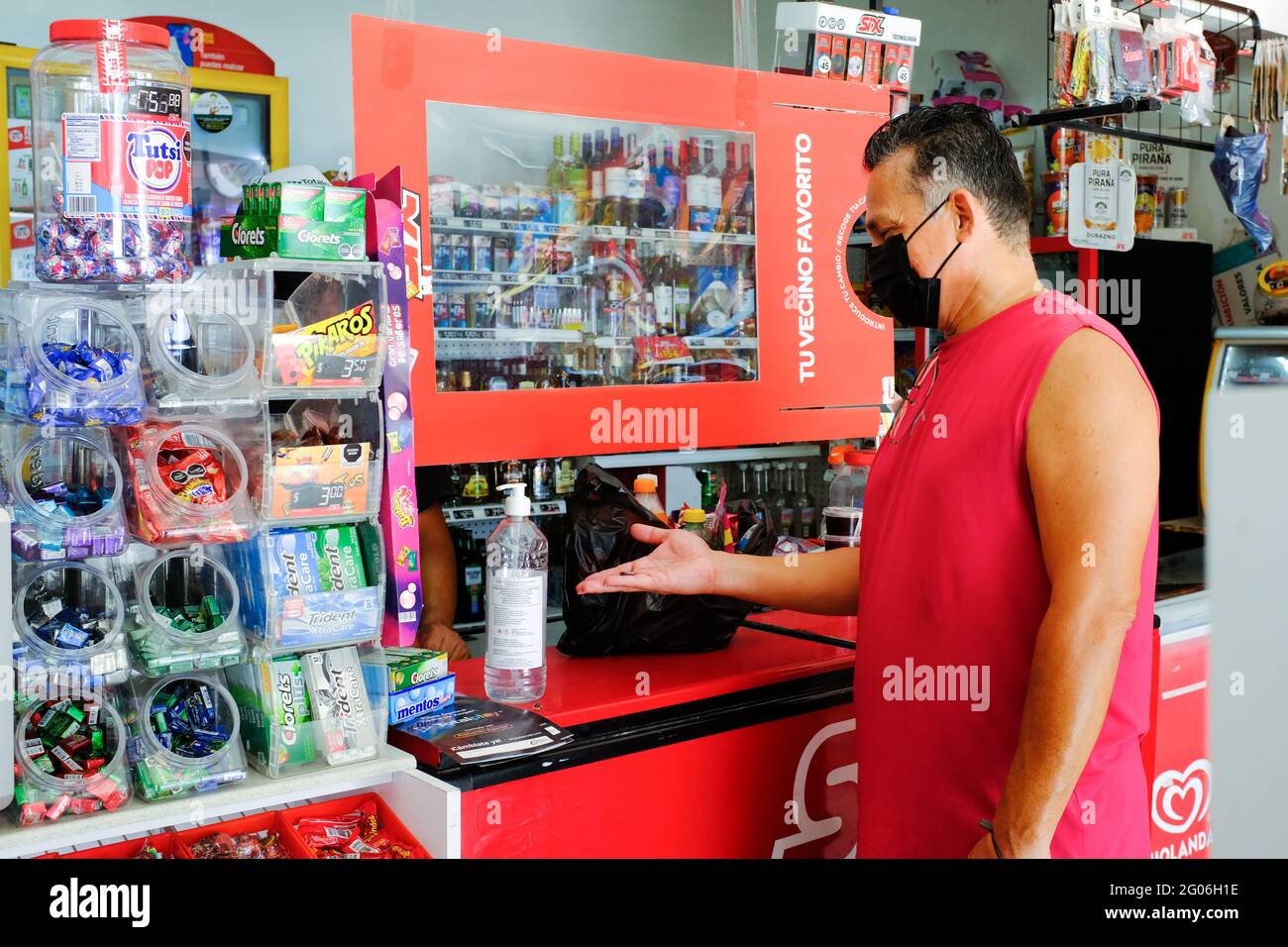 Mann, der in einem kleinen Geschäft in Merida Mexiko Vorräte kauft Während der Covid-19 Pandemie / kann man die Vorsorge beachten Vom Lager ergriffene Maßnahmen (Kunststoffabscheider und Desinfektionsgel) Stockfoto