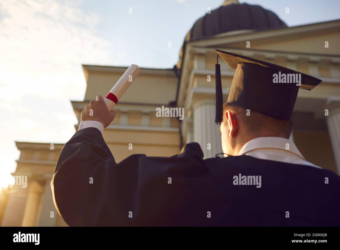 Student in Kleid und akademischen Hut mit Diplom bei der Abschlussfeier angehoben Stockfoto