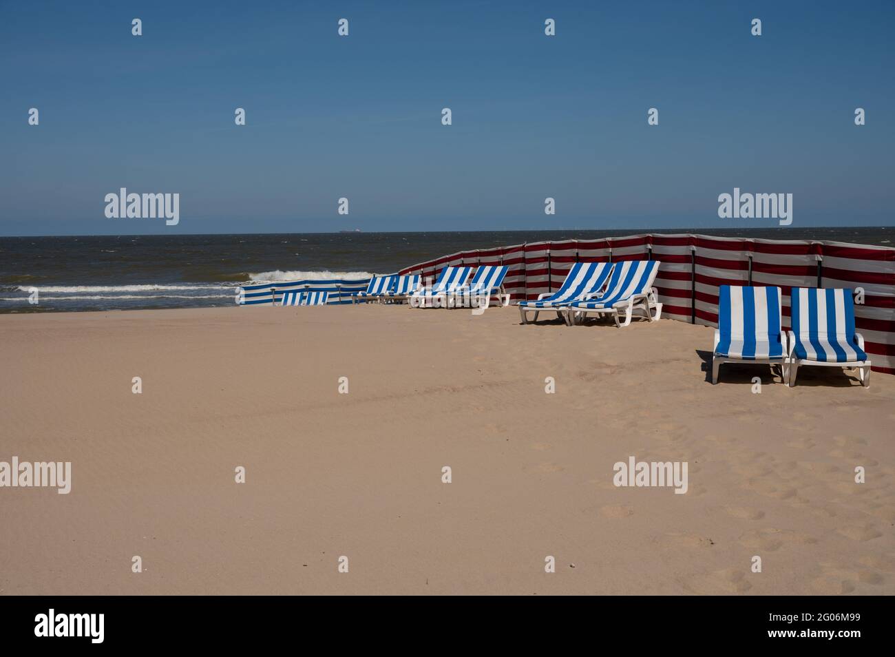 Leere blau-weiße Sonnenliegen am gelben Sandstrand in der kleinen belgischen Stadt De Haan oder Le Coq sur mer, Luxus-Urlaubsziel, Sommerferien Stockfoto