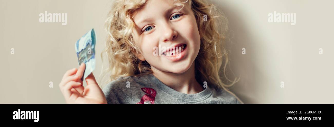 Kaukasisches blondes Mädchen, das ihren fehlenden Zahn im Mund zeigt und Geld von einer Zahnfee hält. Stolzes Kind, das einen verlorenen Zahn zeigt. Aufwachsen Stockfoto