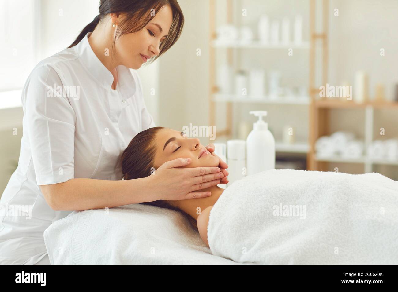 Lächelnder Arzt Dermatologe machen Verfahren der entspannenden Gesichtsmassage für Junge Frau Stockfoto