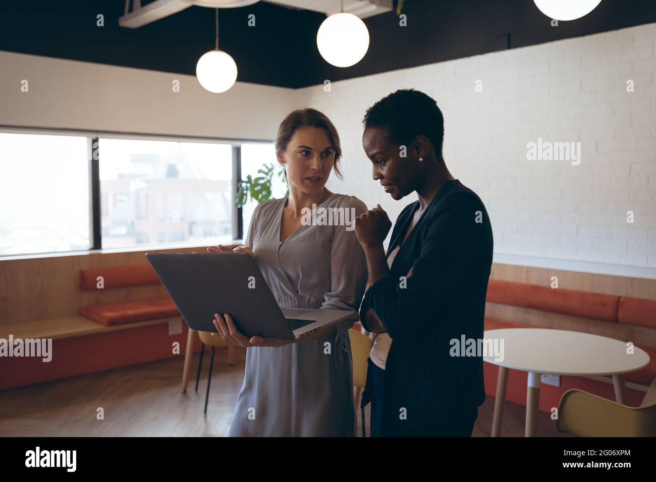 Zwei verschiedene Geschäftsfrauen stehen, reden, benutzen Laptop bei der Arbeit Stockfoto