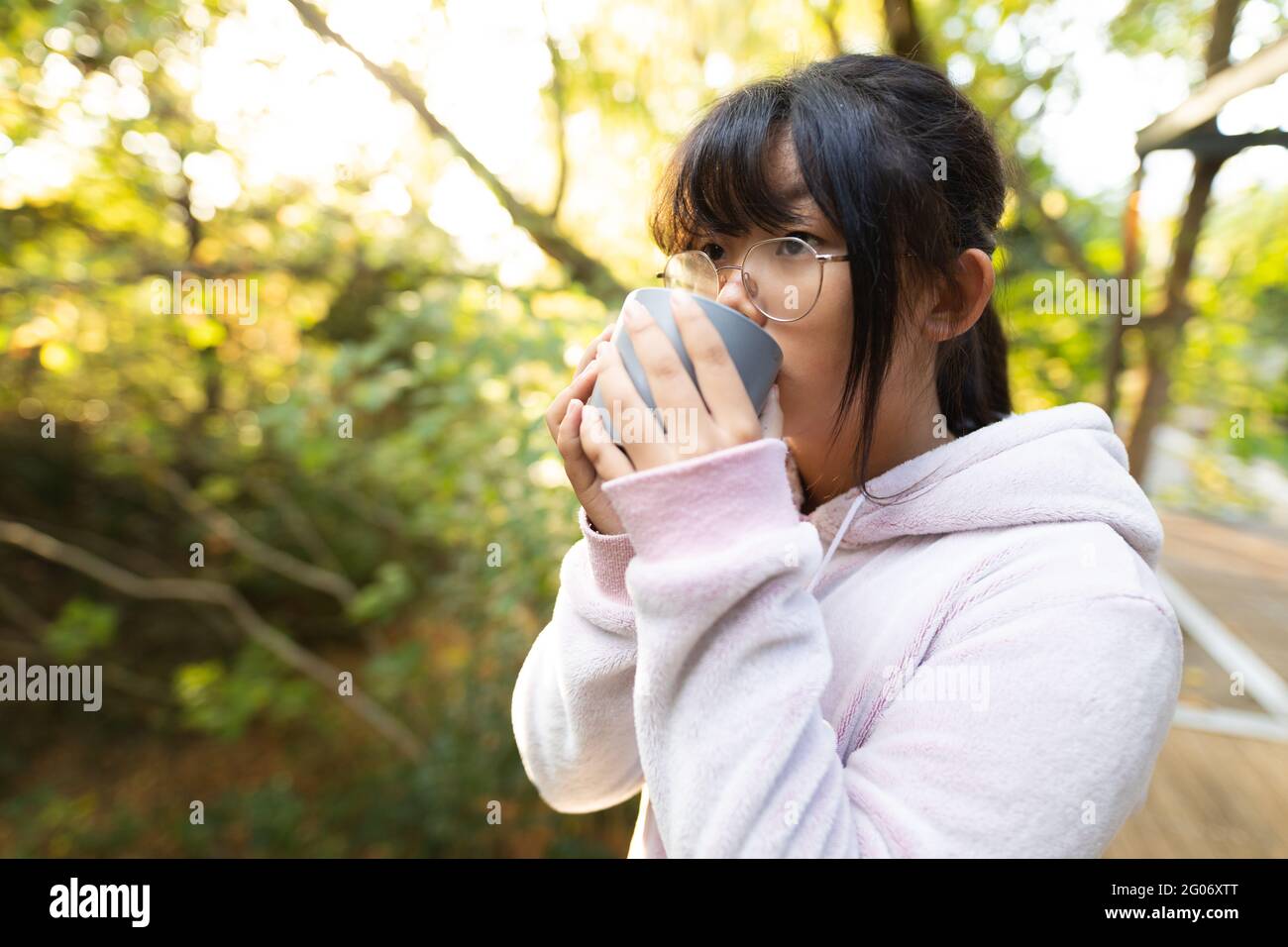 Asiatische Mädchen in rosa Kapuzenpullover trinken Tee im Garten stehen Stockfoto