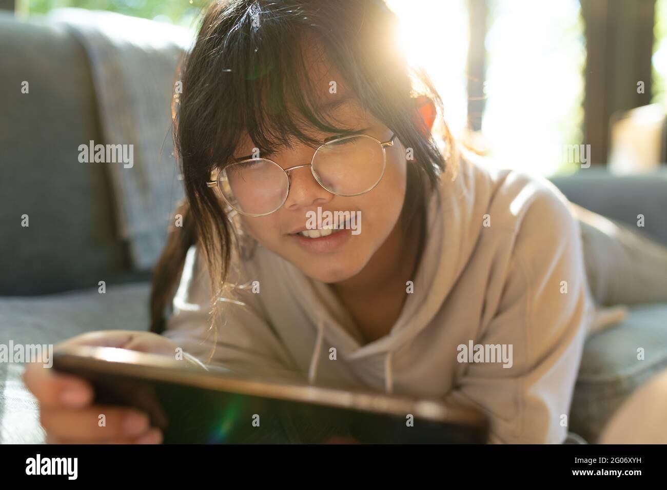 Lächelndes asiatisches Mädchen in Brille mit Smartphone und liegend auf dem Sofa Stockfoto