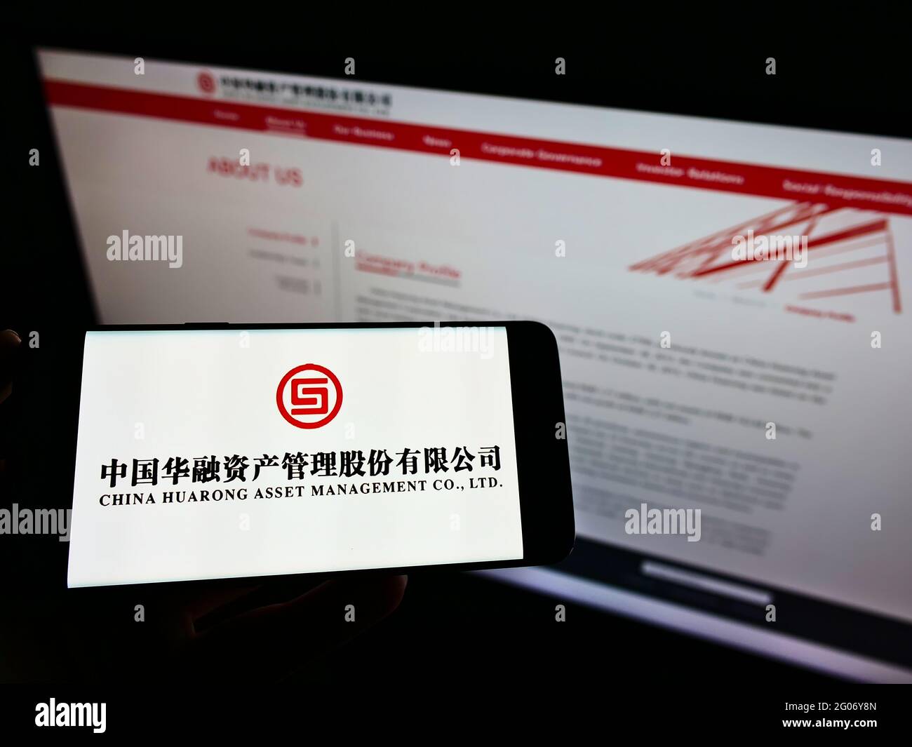 Person, die Mobiltelefon mit dem Logo von China Huarong Asset Management Co. Ltd. Auf dem Bildschirm vor der Business-Webseite hält. Konzentrieren Sie sich auf die Telefonanzeige. Stockfoto
