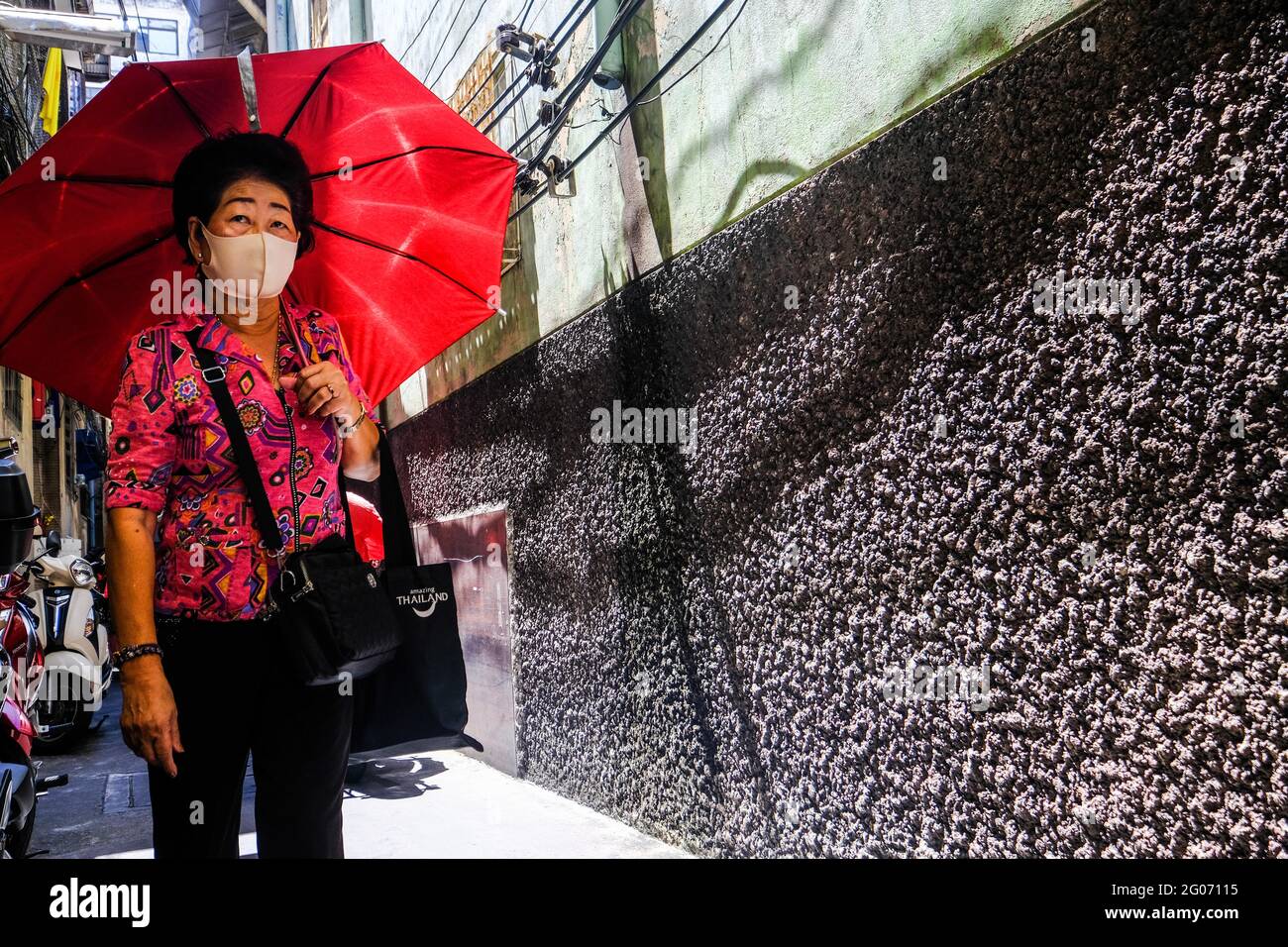 Eine Frau mit einem roten Regenschirm geht entlang einer sonnendurchfluteten Gasse in Chinatown, Bangkok, Thailand Stockfoto