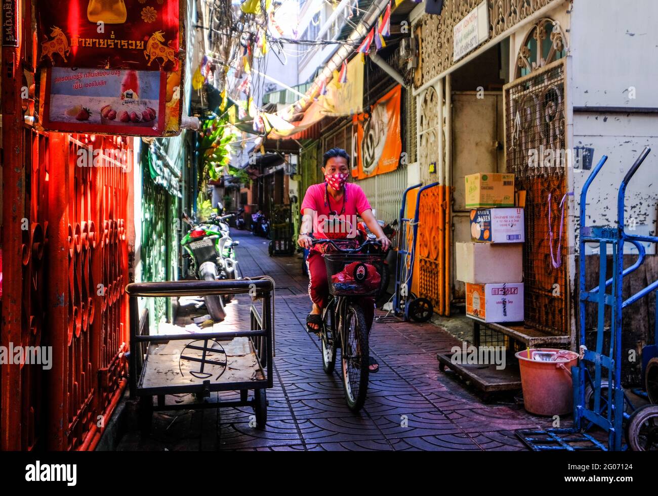 Eine Radfahrerin fährt durch eine farbenfrohe Gasse in der Chinatown-Gegend von Bangkok, Thailand Stockfoto