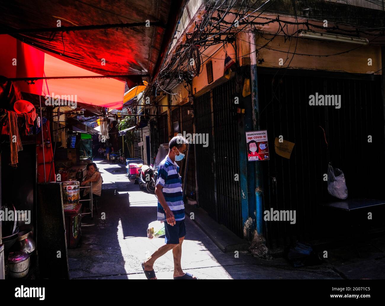 Ein Mann geht durch eine sonnendurchflutete Gasse in Chinatown, Bangkok, Thailand Stockfoto