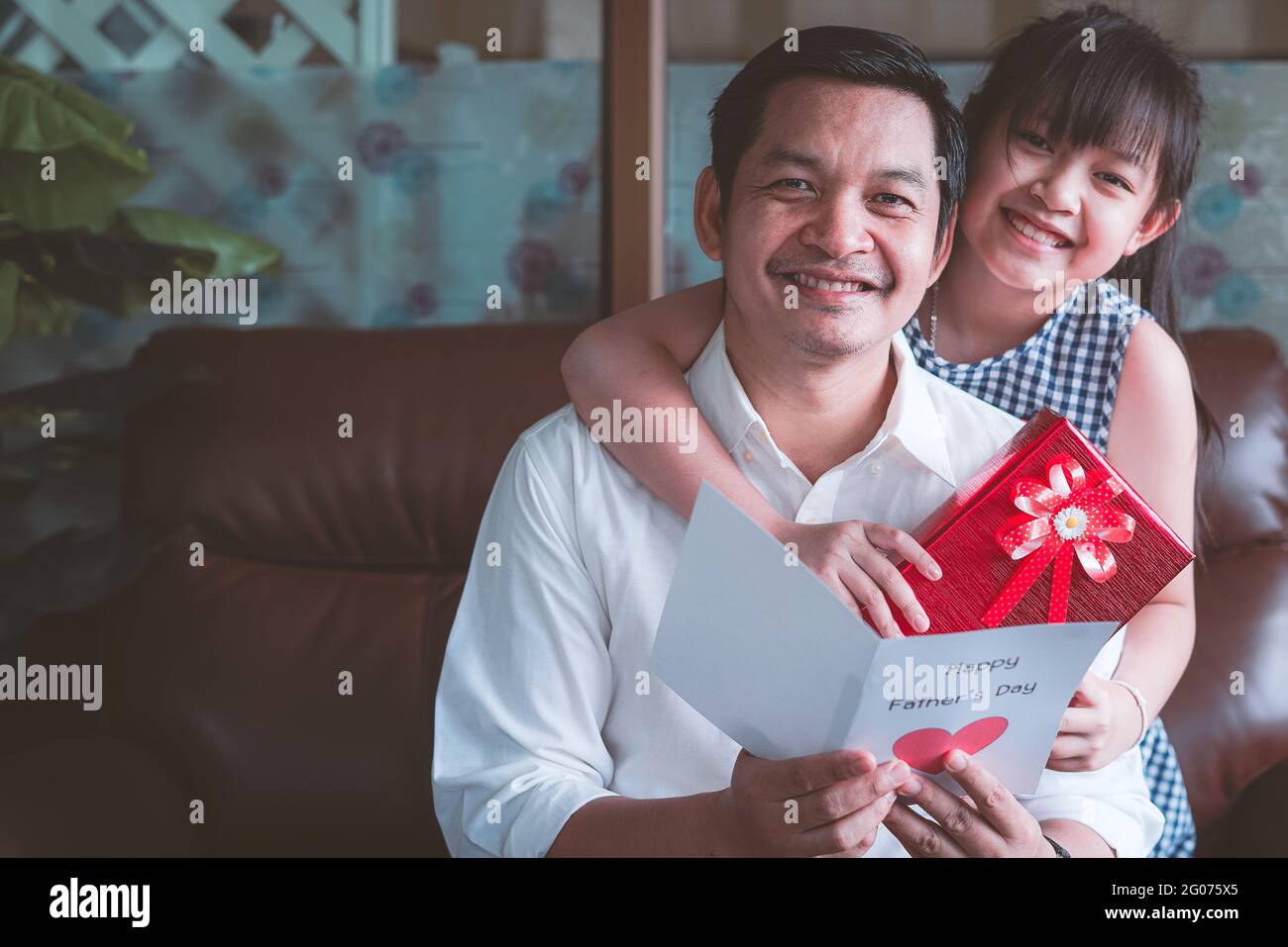 Asiatische kleine Kinder Töchter gratulieren Vater und geben ihm Postkarte Und Geschenkbox mit lächelnd und umarmend.Konzept der glücklichen Vaters Tag Stockfoto