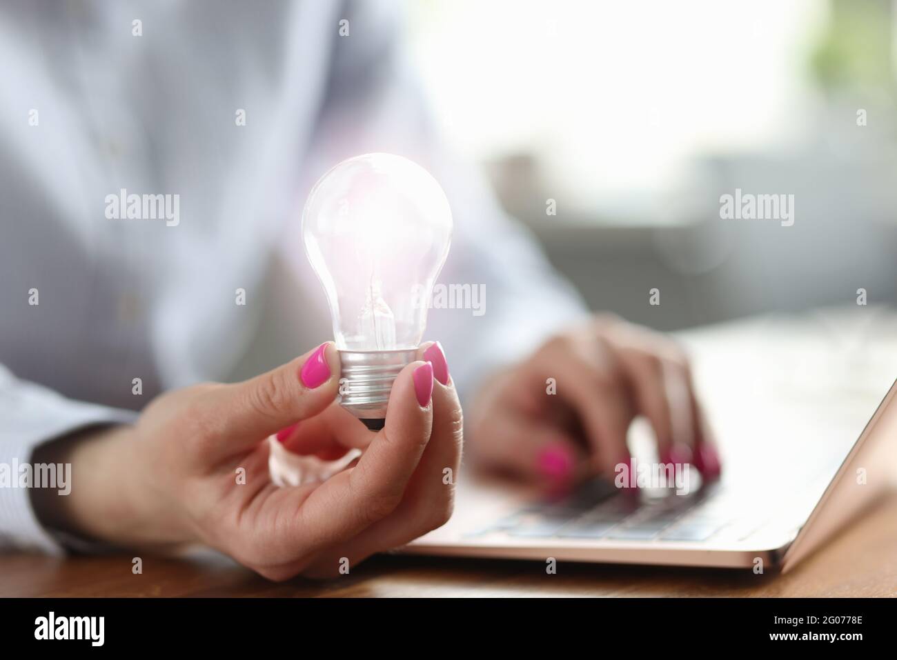 Frau hält Glühbirne in der Hand und arbeitet am Laptop Stockfoto