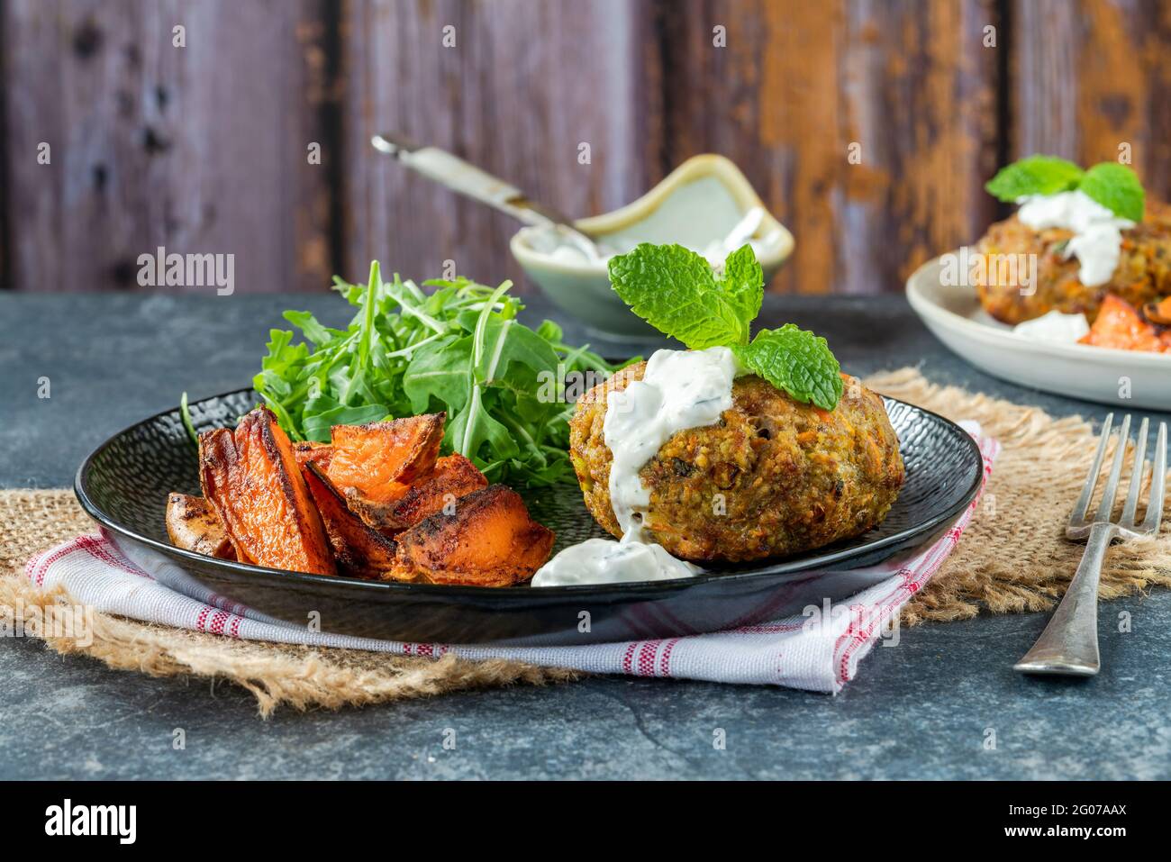 Lamm-, Karotten-, Couscous- und Minzburger mit würzigen Süßkartoffelkeilen und Rucola-Salat Stockfoto