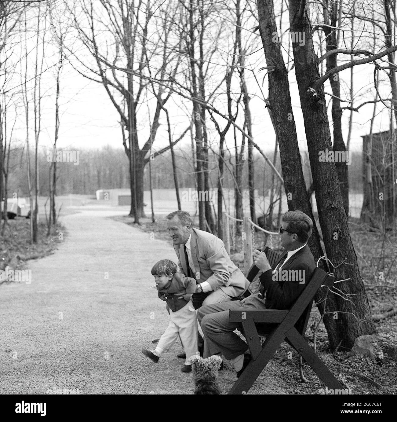 31. März 1963 Wochenende im Camp David. Unter dem Navy-Minister holt Paul „Red“ Fay John F. Kennedy, Jr., ab, während Präsident Kennedy und der Hund von Kennedy, Charlie, sich aufmachen, Camp David, Maryland. Stockfoto