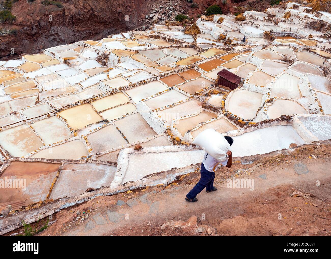 Peruanischer Salzporter auf den Salzterrassen von Maras mit großen Säcken Salz, Cusco, Peru. Stockfoto