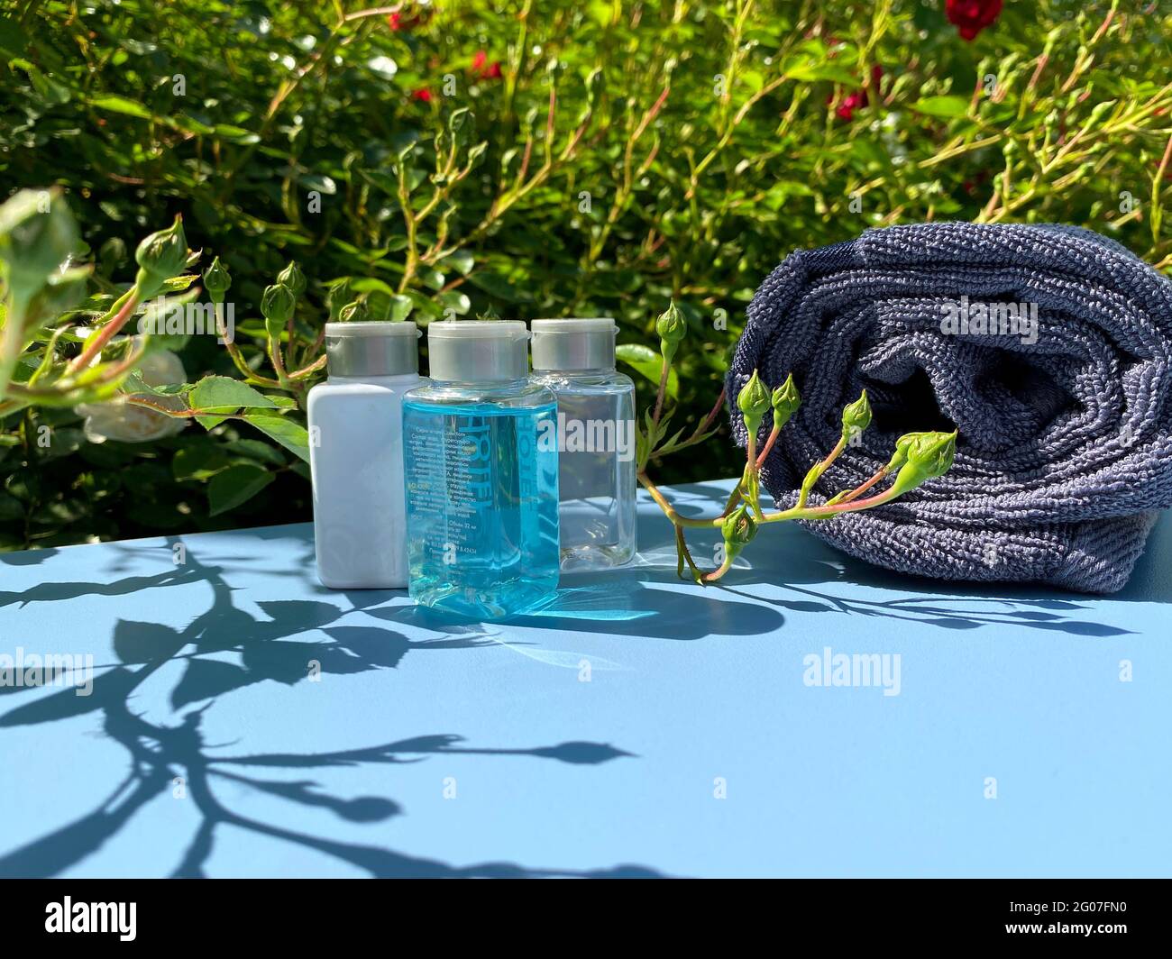 Mini-Flaschen mit Kosmetikprodukten und Handtuch auf blauem Hintergrund mit Blättern und Schatten. Hotelannehmlichkeiten SPA und REISEKONZEPT. Stockfoto