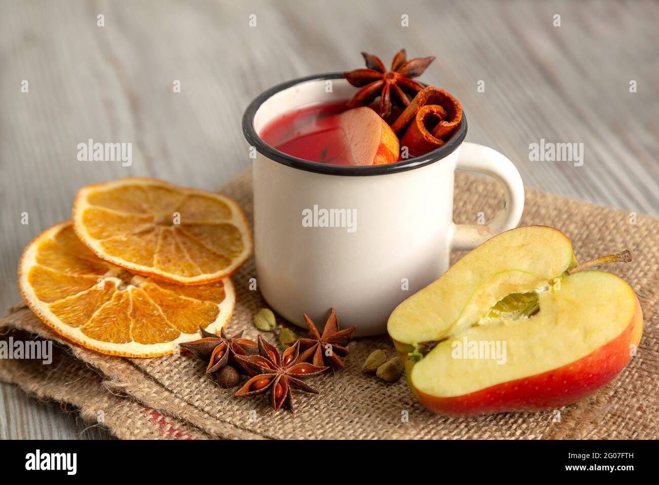 Glühwein in weißem Becher mit Früchten und Gewürzen auf Holzgrund. Traditionelles weihnachtliches Heißgetränk mit Rotwein, Äpfeln, Orangen, Anise Stockfoto