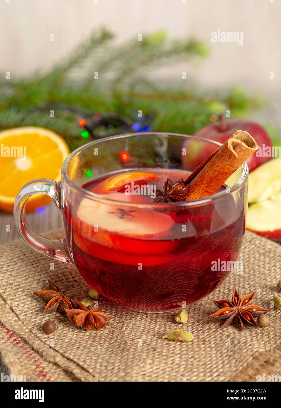 Glühwein mit Gewürzen und Früchten auf einem Holztisch. Heißer Weihnachtsdrink mit Rotwein, Äpfeln, Orangen und Zimt. Traditionelle Feiertagskarte. Stockfoto