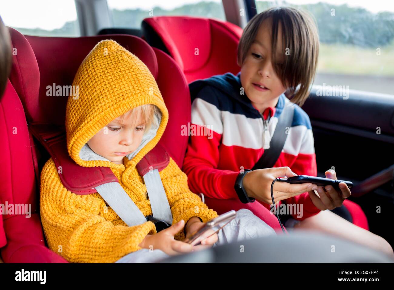 Drei Kinder, Jungen, die im Auto im Carseat unterwegs sind und auf Handys spielen, um die Zeit zu verkürzen Stockfoto