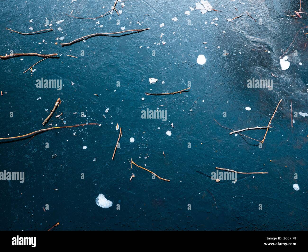 Die Eisoberfläche eines gefrorenen Sees ist mit trockenen Ästen bedeckt. Winterhintergrund. Stockfoto