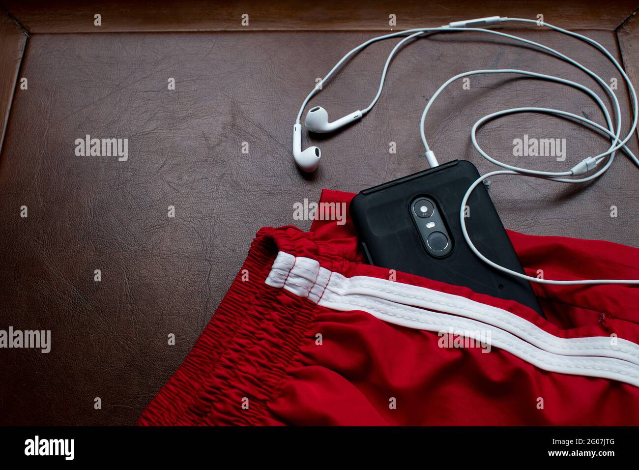 Schwarzes Smartphone, Kopfhörer und rote kurze Hose für den Sommer auf  einem braunen Holztisch Stockfotografie - Alamy