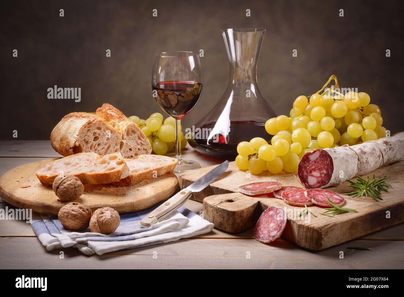 Salami, Brot, Trauben, Walnüsse und Rotwein mit Dekanter in rustikalem Ambiente. Stillleben, Raum für Text. Stockfoto