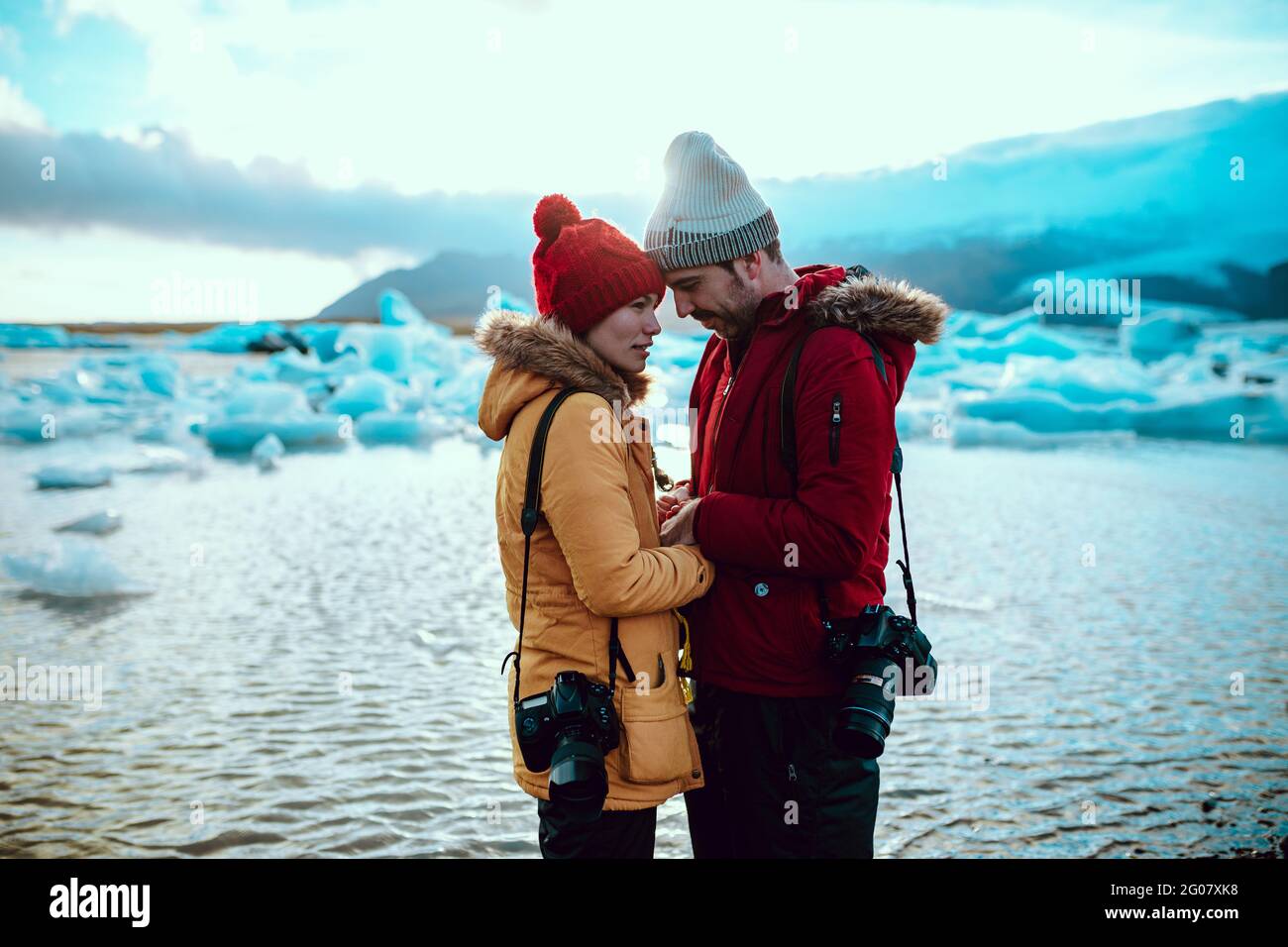 Seitenansicht des jungen Mannes und der Frau im Winter mit professionellen Kameras, die am Ufer in der Nähe des Wassers mit Eis stehen Stockfoto