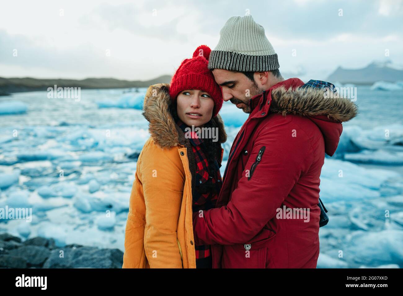 Seitenansicht des jungen Mannes und der Frau im Winter mit professionellen Kameras, die am Ufer in der Nähe des Wassers mit Eis stehen Stockfoto