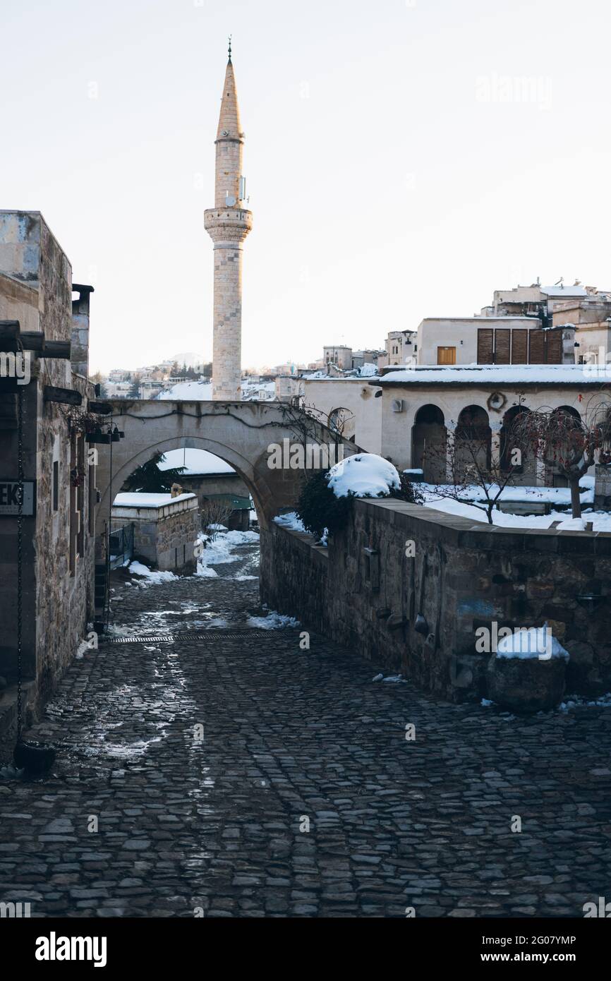 Leere Straße mit Pflastersteinen führt zwischen alten Gebäuden zu Hoher Minarett-Turm gegen klaren blauen Himmel in der Türkei Winterzeit Stockfoto