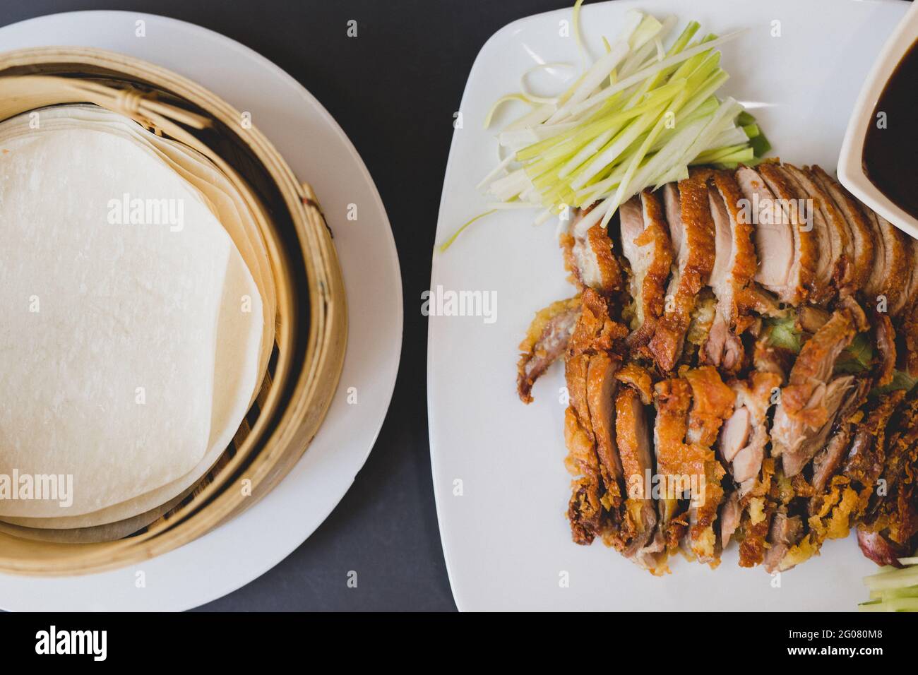 Von oben Zusammensetzung aus geschnittener Pekinger Ente auf weißer Keramik Teller mit traditionellen Bambus-Dampfgarern Stockfoto