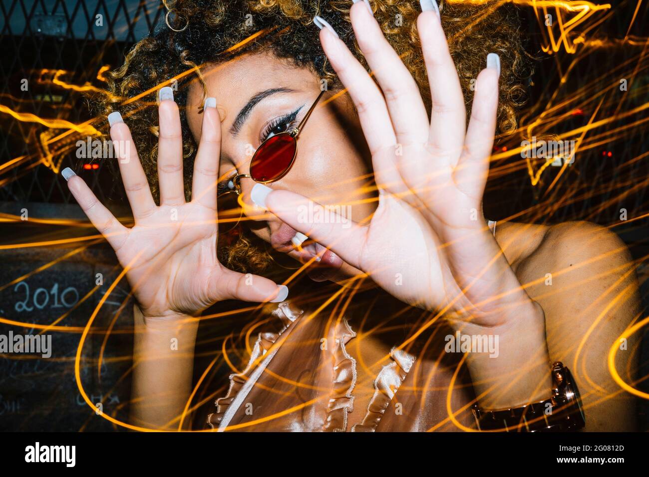 Ausdrucksstarke junge ethnische Dame mit Afro-Haaren in stilvoller Sonnenbrille Und oben berühren Kopf und laut schreiend, während sie sich abkühlen Nachtclub in der Nähe von Freeze l Stockfoto