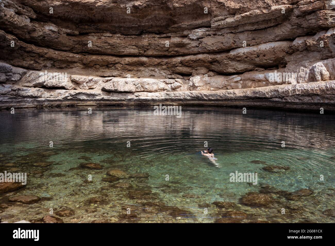 Entspannte, anonyme Frau, die auf dem transparenten Wasser des Bimmah-Sinkholes schwimmt, umgeben von rauen Felsen, während einer Reise in den Oman Stockfoto