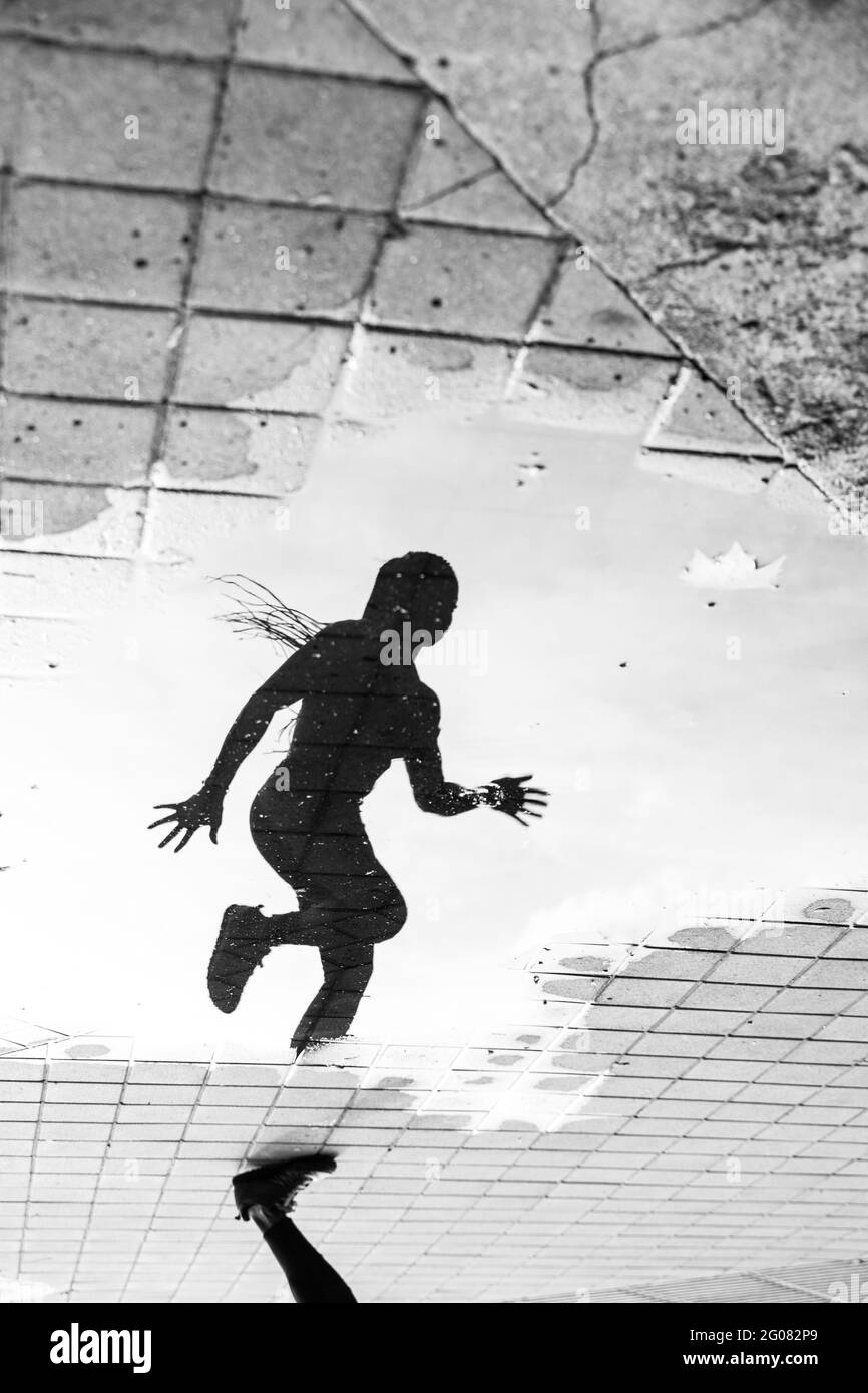 Crop Bein und Reflexion in Paddel von Wasser der anonymen Weibliche Sportlerin, die während des Outdoor-Workouts auf der Stadtstraße läuft Stockfoto
