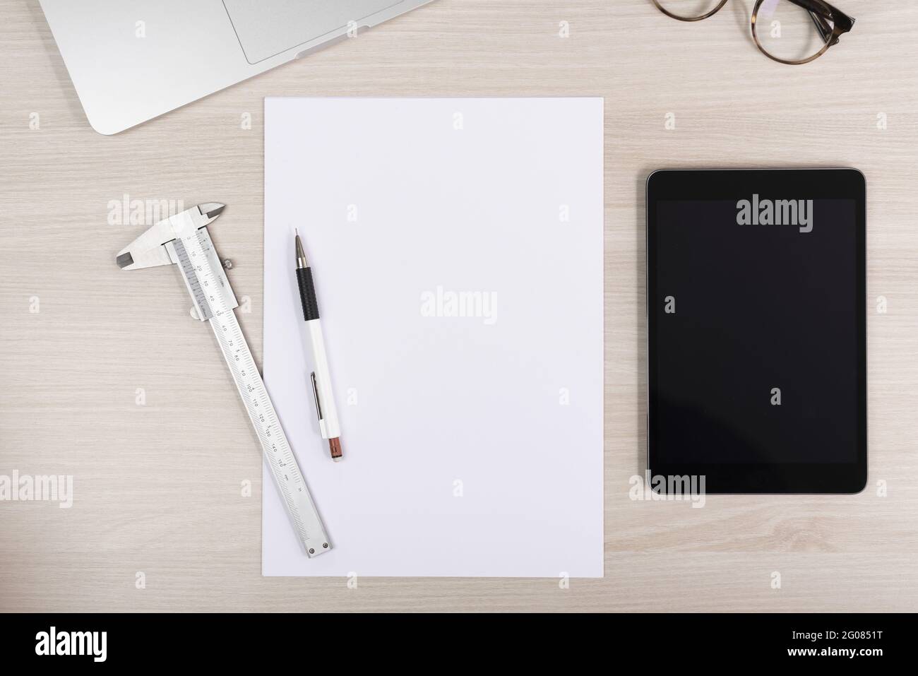 Draufsicht auf den Arbeitsplatz eines Geschäftsmannes mit Papieren, Stift, Messschieber, Tablet und Brille Stockfoto