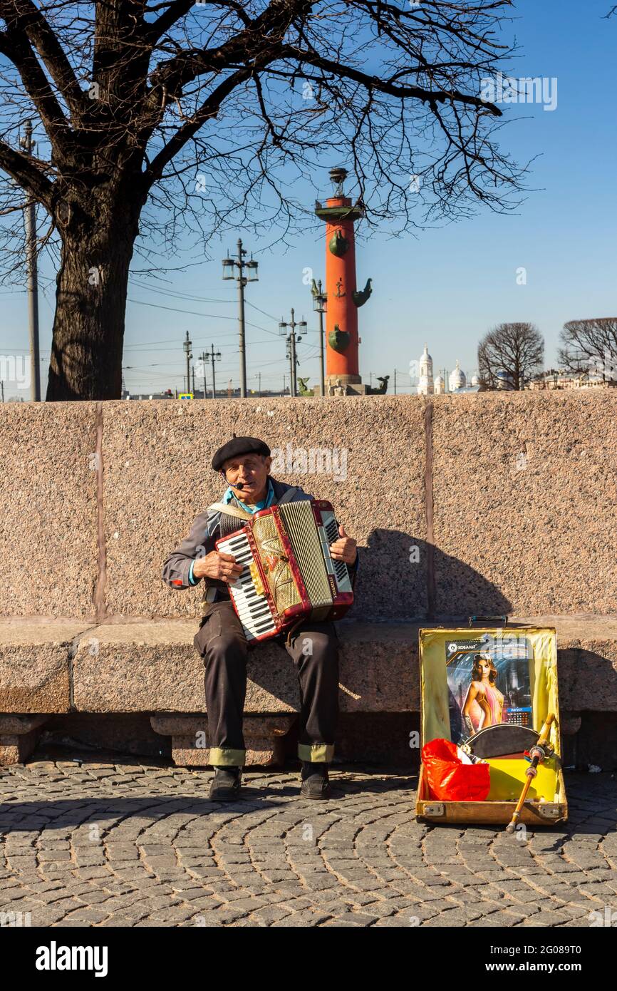 Ein Straßenmusiker spielt am Spieß der Insel Vasiliewski ein Akkordeon. Im Hintergrund befindet sich eine Rostral-Säule. Russland St. Petersburg. Stockfoto