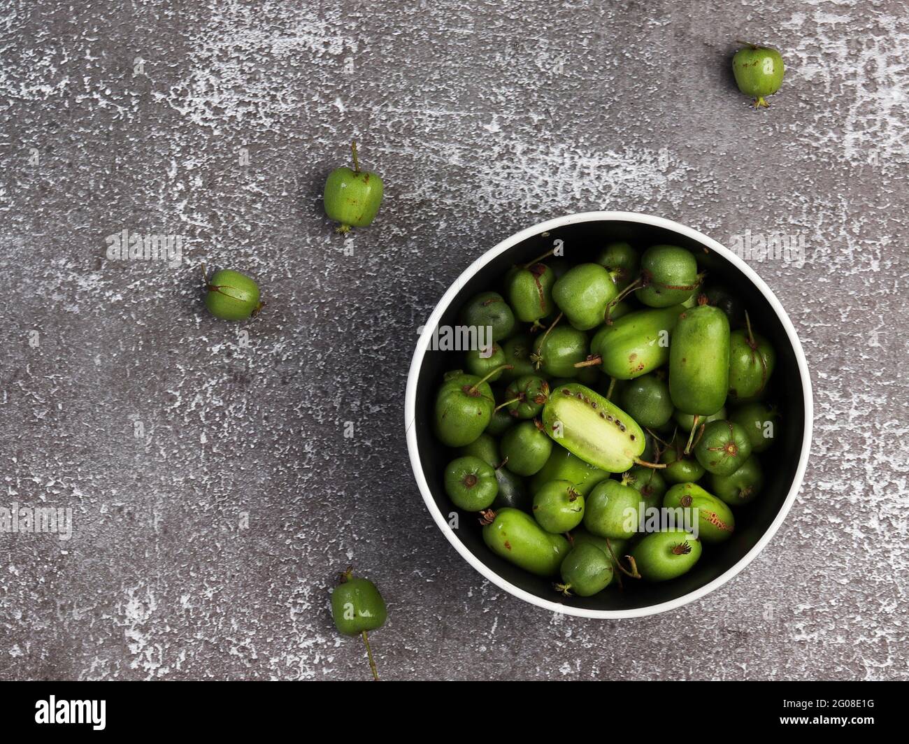 Mini-Kiwi-Babyfrucht (Actinidia arguta) in einer Schüssel auf dunklem Grund. Draufsicht, flach liegend Stockfoto