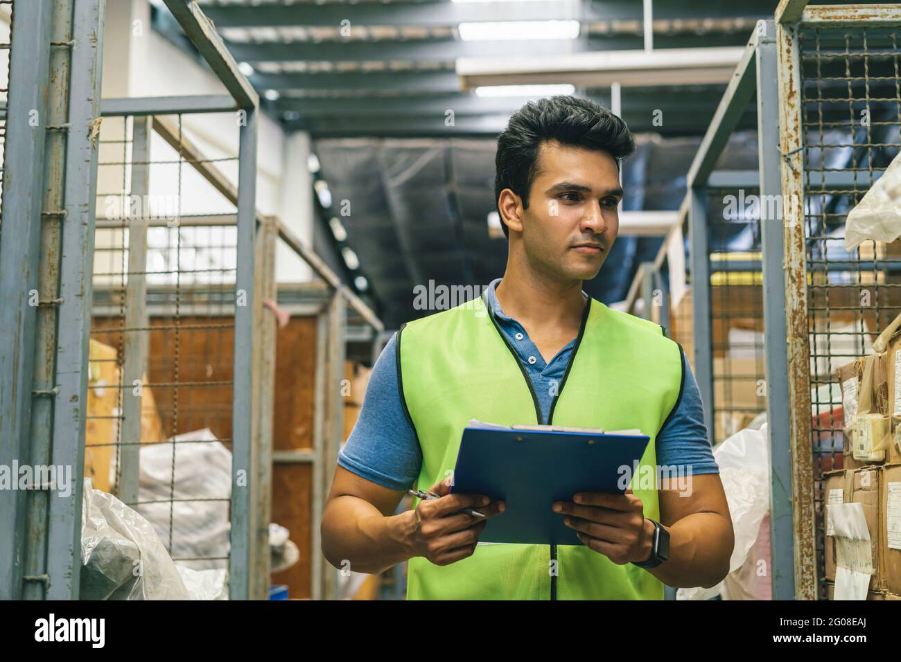 20s indischen Verteilung Versand Depot Arbeiter zu Fuß und überprüfen Sie den Bestand. Männlicher Arbeiter in Arbeitsuniform im Lagerhaus. Logistik Versandzentrum Karrierekonzept - Rückansicht Stockfoto