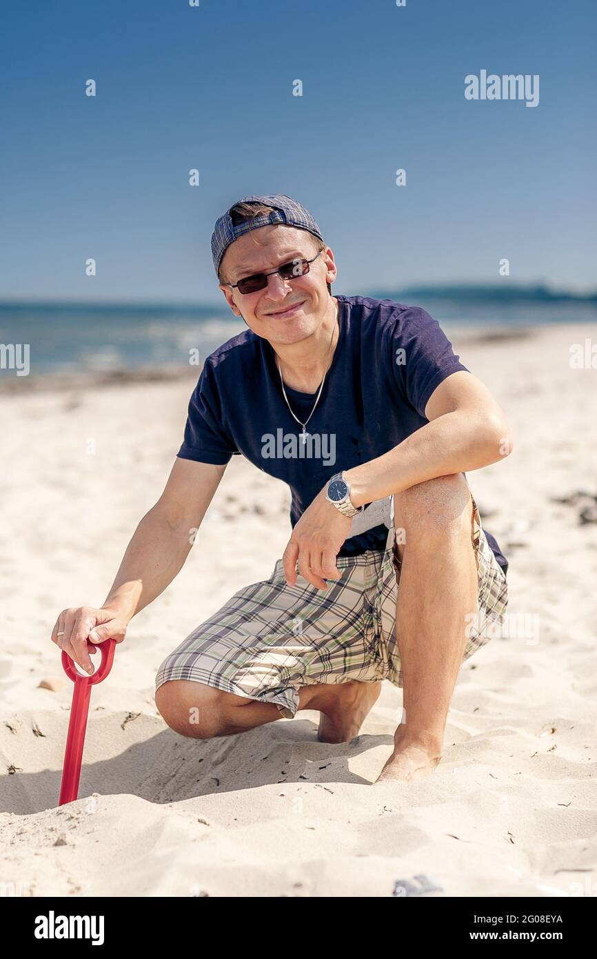 Vater hält Plastikschaufel mit Sand am Strand des Meeres Stockfoto