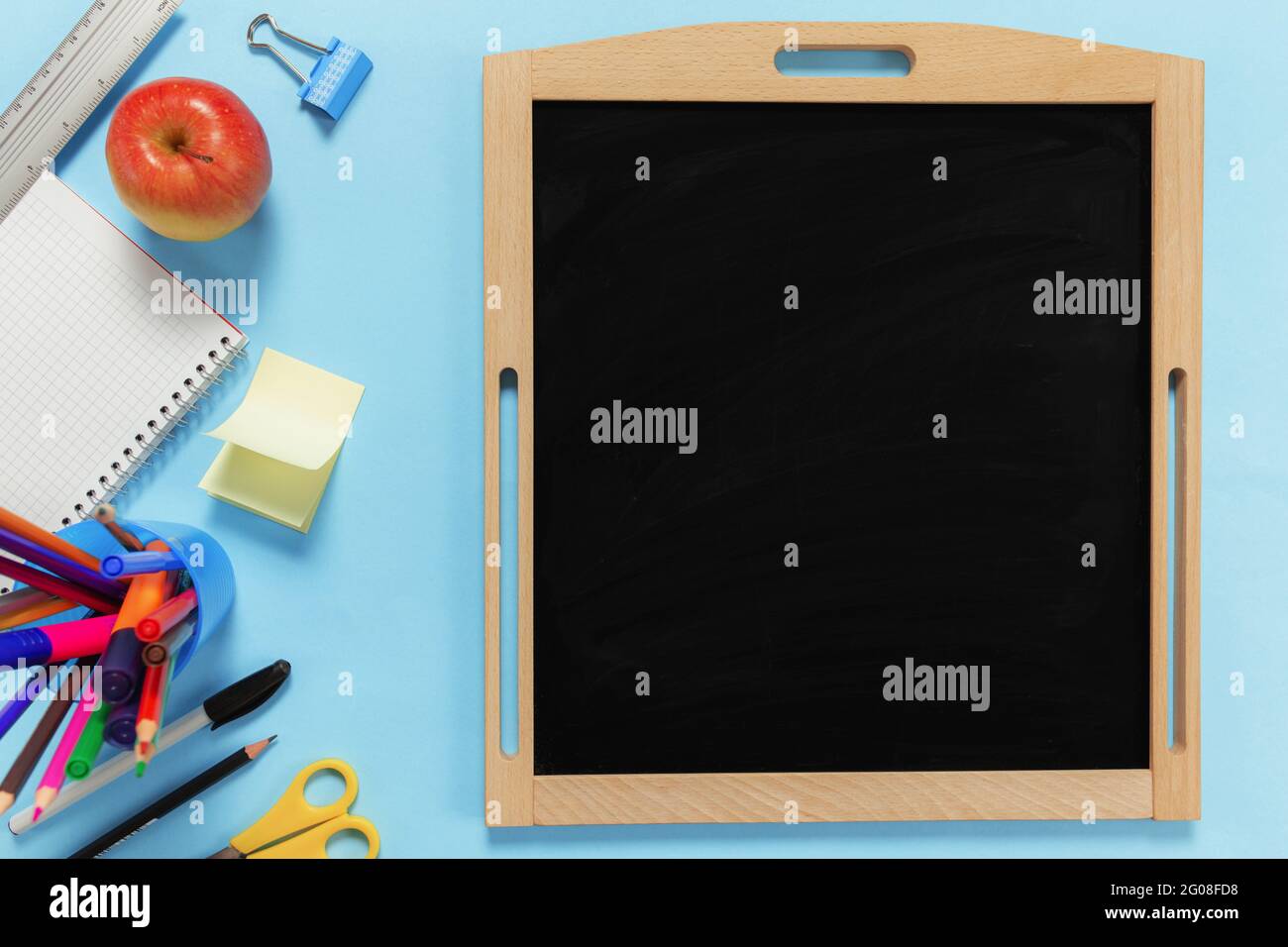 Flat Lay mit Schulkonzept auf blauem Hintergrund mit verschiedenen Schulzubehör, Stiften, Bleistift, Notizblock, Büroklammern, apfel, Lineal, Schere, leer Stockfoto