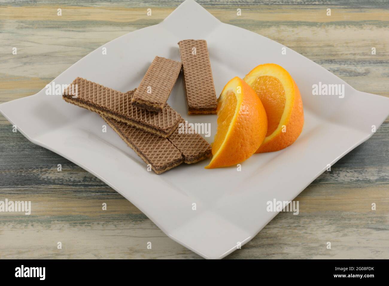 Orangen- und Kakaocreme-Waffeln, Kekse und Orangenscheiben auf weißem Dessertteller Stockfoto