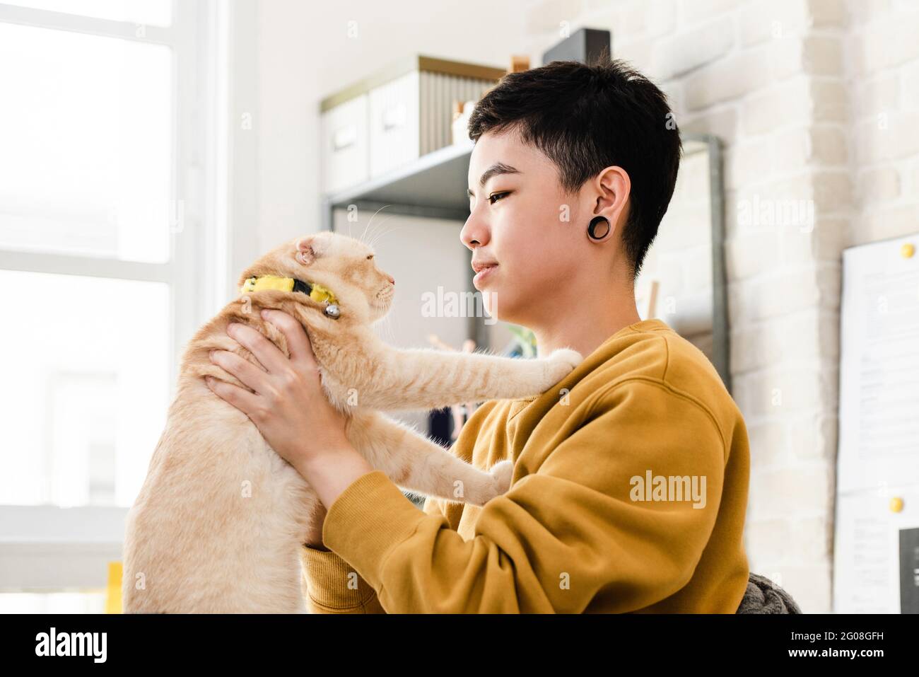 Junge asiatische Tomboy Frau in lässiger Kleidung hält und schaut ihre Katze liebevoll an Stockfoto