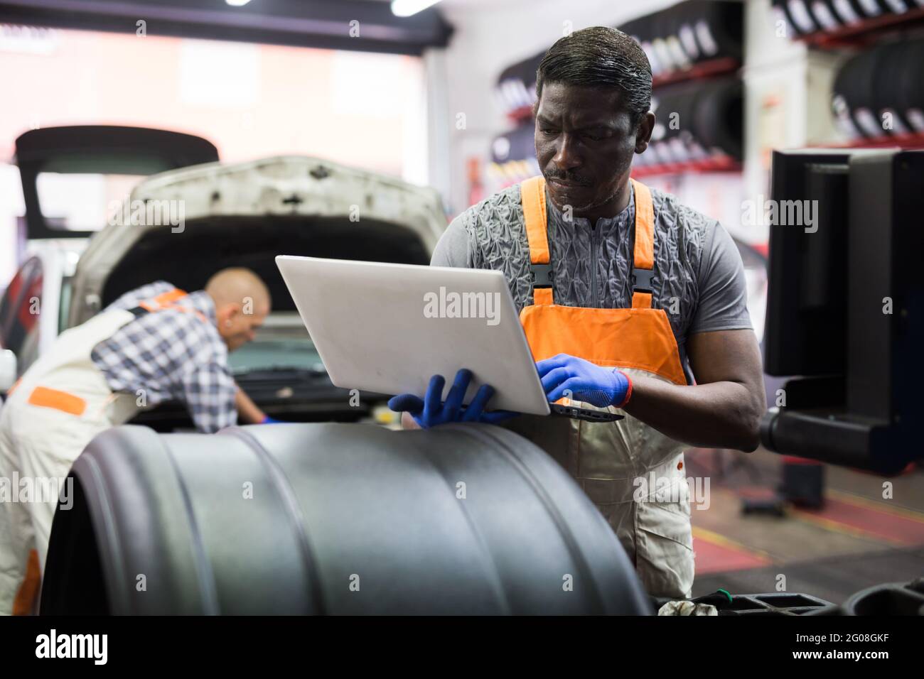 Afrikanischer Mechaniker, der in der Werkstatt ein Auto mit einem Laptop überprüft Stockfoto