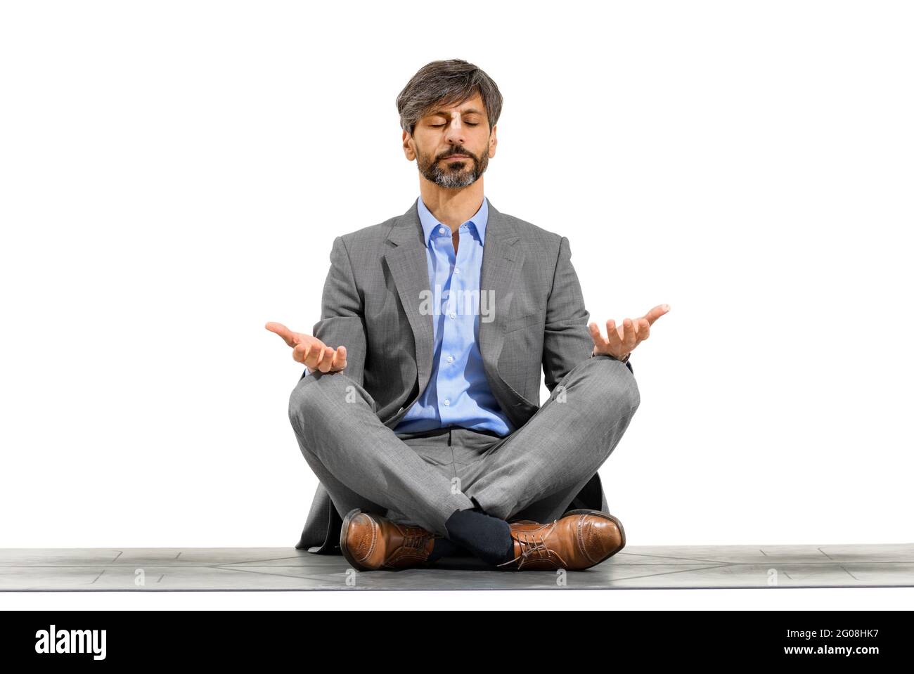 Eleganter Geschäftsmann, der in der Yoga-Lotus-Pose meditiert, sitzt auf einer Übungsmatte mit geschlossenen Augen und einem ruhigen Ausdruck, isoliert über einer weißen Studio-BA Stockfoto