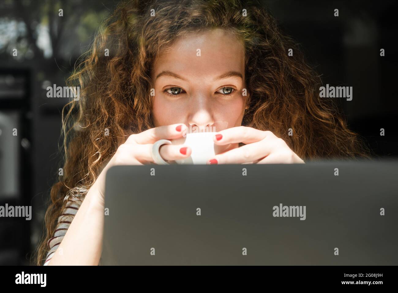 Junge kaukasische Frau, die Kaffee trinkt, während sie sich am frühen Morgen ein Video auf einem Laptop-Computer zu Hause ansieht Stockfoto