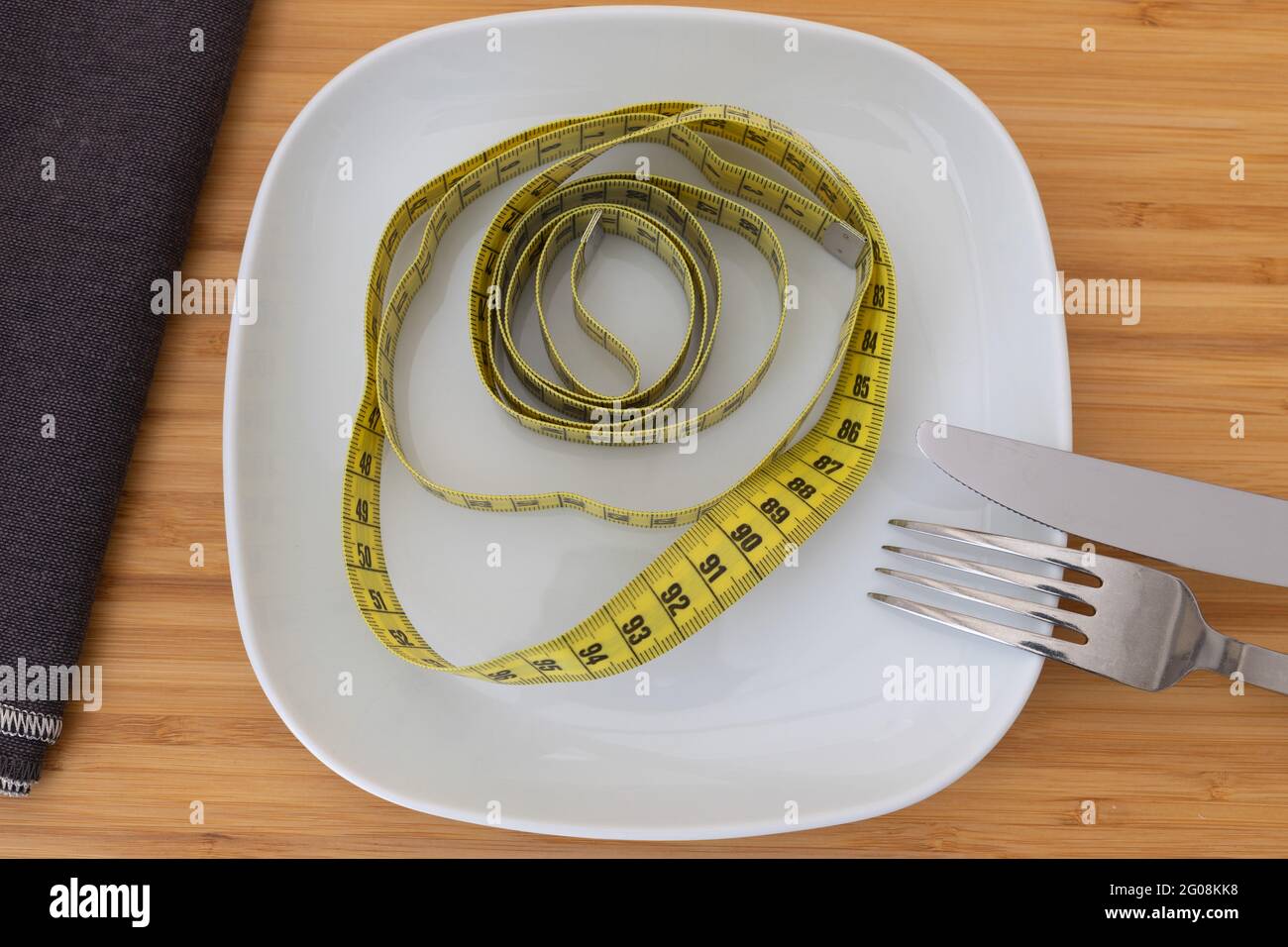 Draufsicht auf ein Maßband auf einem weißen Teller mit Besteck als Konzept für Diätkost Stockfoto