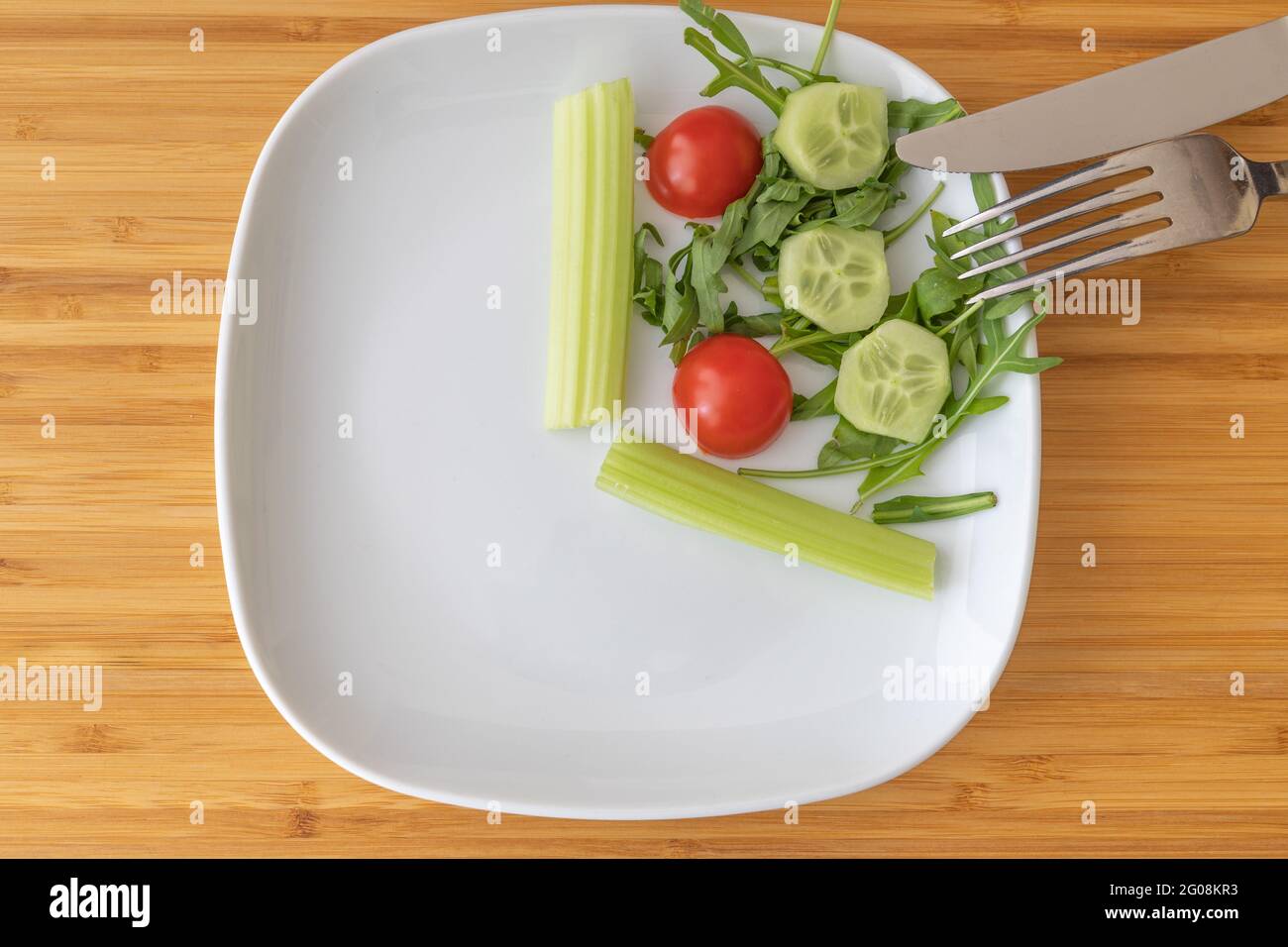 Draufsicht auf Salat auf weißem Teller mit Besteck als Konzept für intermittierendes Fasten Stockfoto