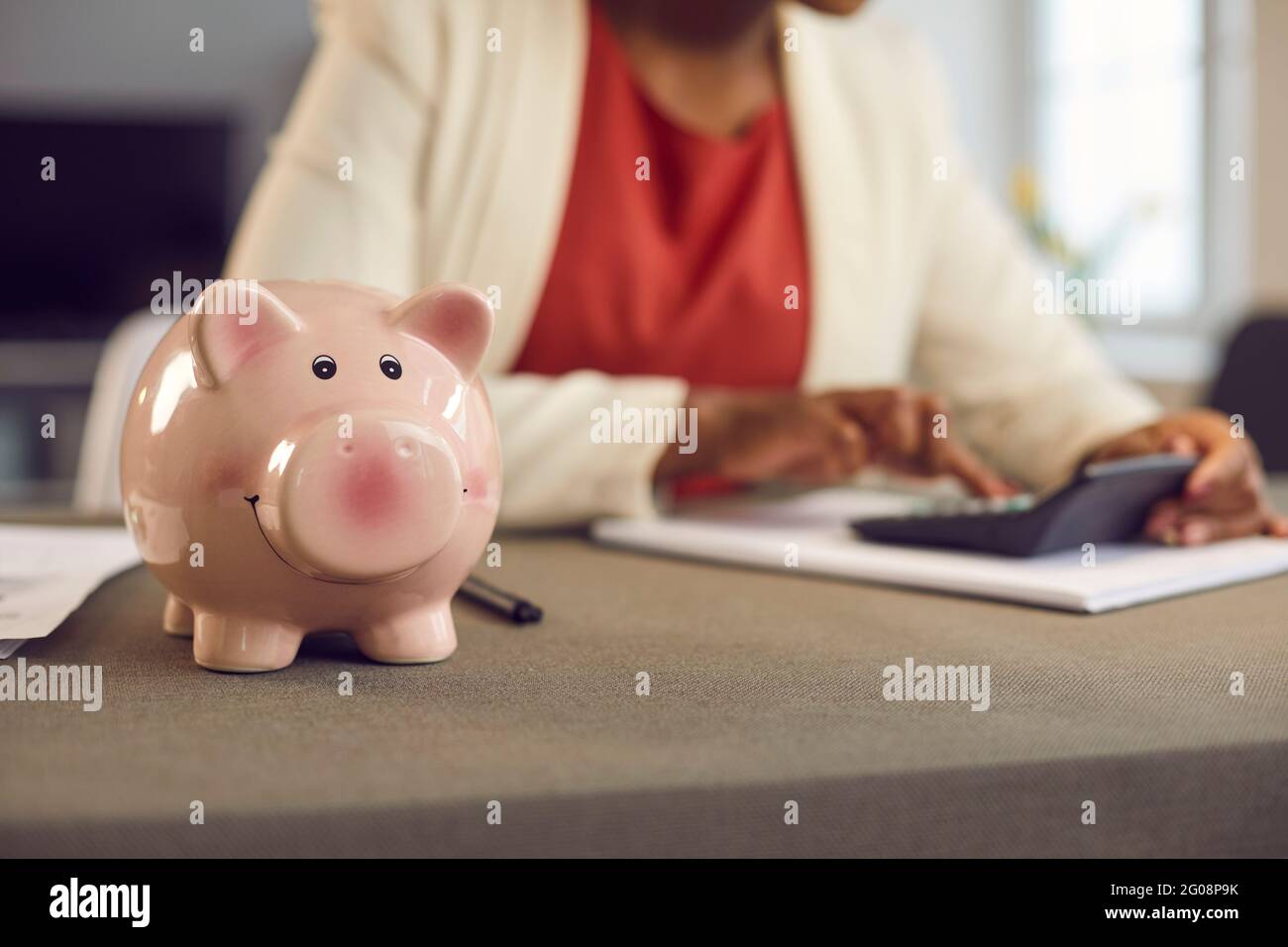 Sparschwein auf dem Tisch aus der Nähe, Frau, die im Hintergrund Einsparungen oder Geschäftsgewinne berechnet Stockfoto